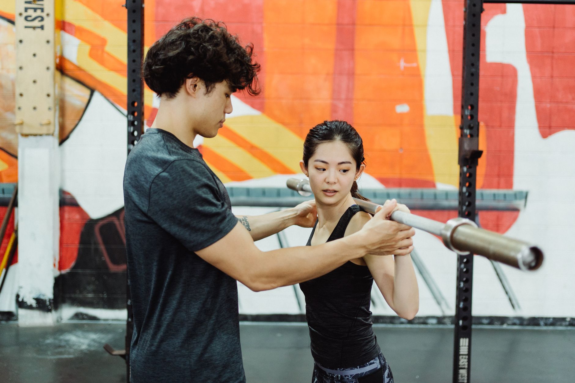 A personal trainer guides a client lifting a barbell, focused on technique and strength training.