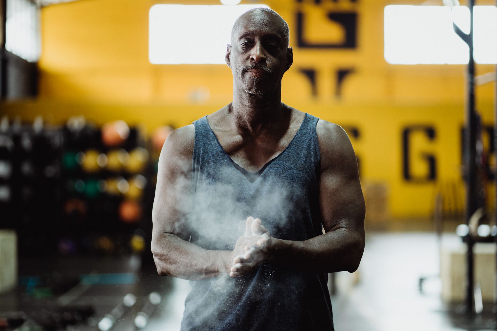 Brawny man in a gym claps powdery hands, ready to lift weights.